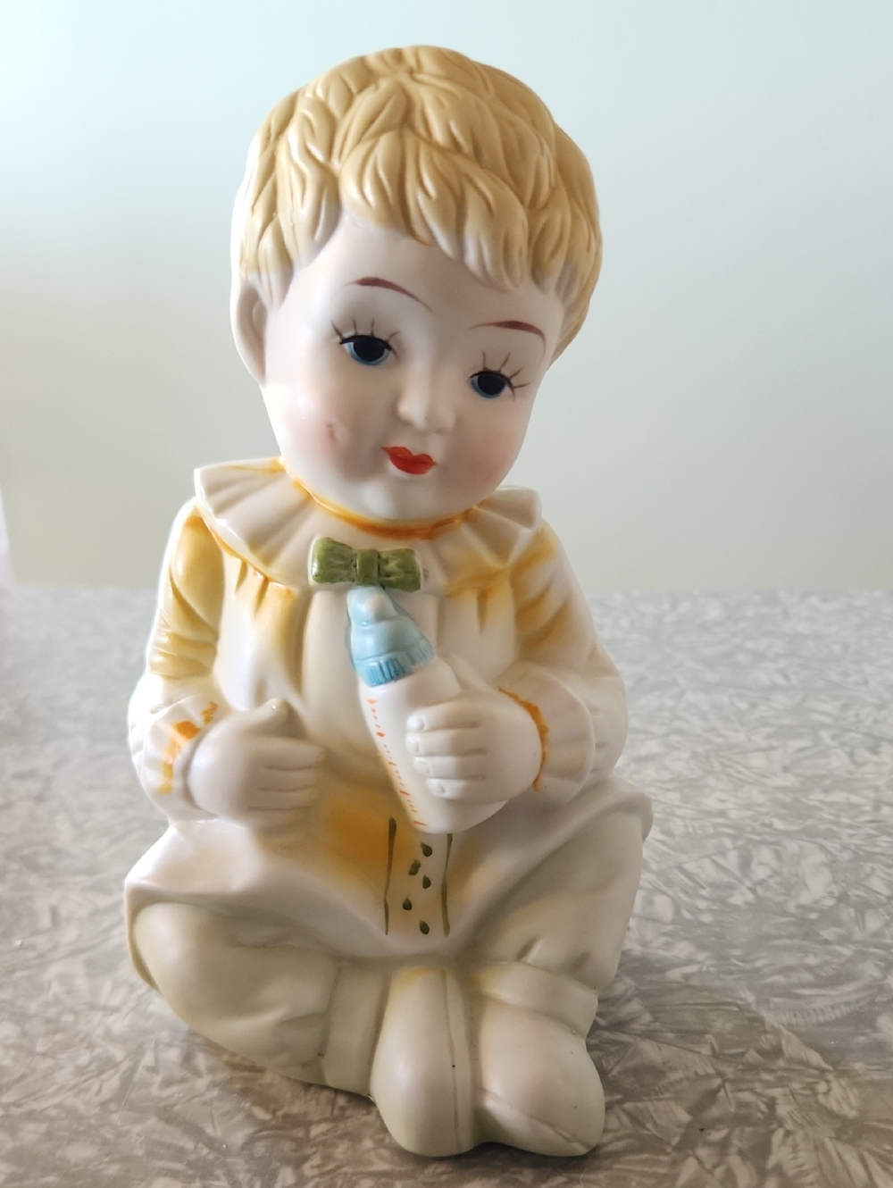 Hand-Painted Porcelain Baby Figurine in Cream and Yellow with Blue Bottle